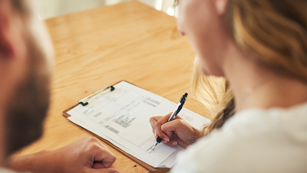 Shot of a young couple signing a document together at home