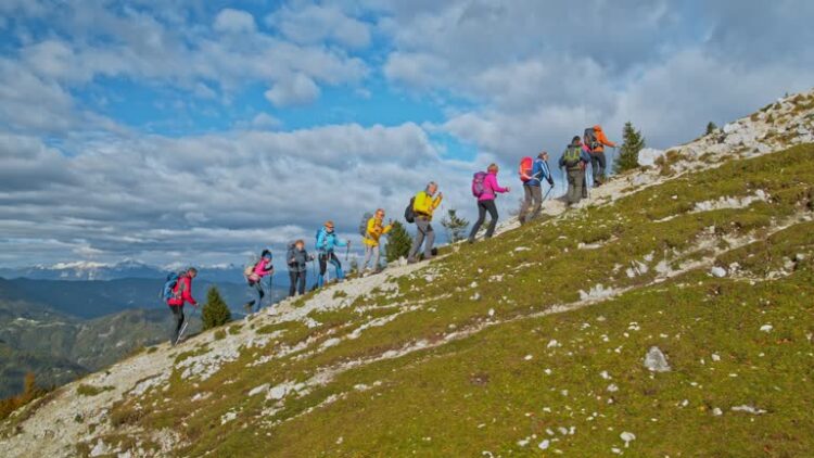 Aerial shot of a group of people hiking up a sunny mountain slope. Shot in Slovenia.