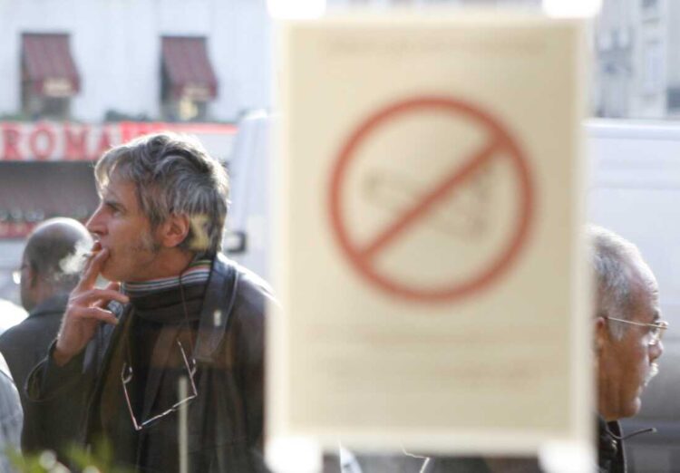 A man smokes a cigarette outside a brasserie, in front of a sticker on a window reading: "Smoking is forbidden," Wednesday, Jan. 2, 2008 in Paris. France's most drastic measure to curb smoking went into effect Wednesday with a full ban on lighting up in cafes, restaurants and discotheques, a sea change for a country where the cigarette first found its place as a potent lifestyle symbol. (AP Photo/Jacques Brinon)
